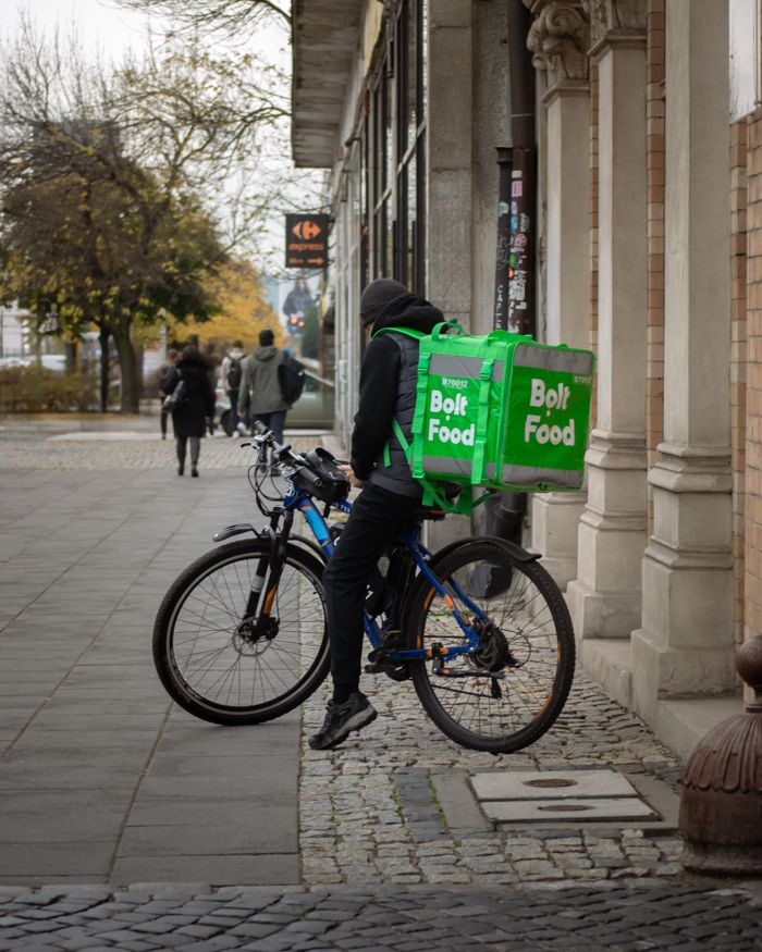 A cyclist delivers food on a city street with a Bolt Food backpack, capturing urban lifestyle.