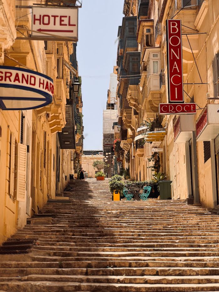 Picturesque view of a sunny, narrow street in Valletta with local shops.