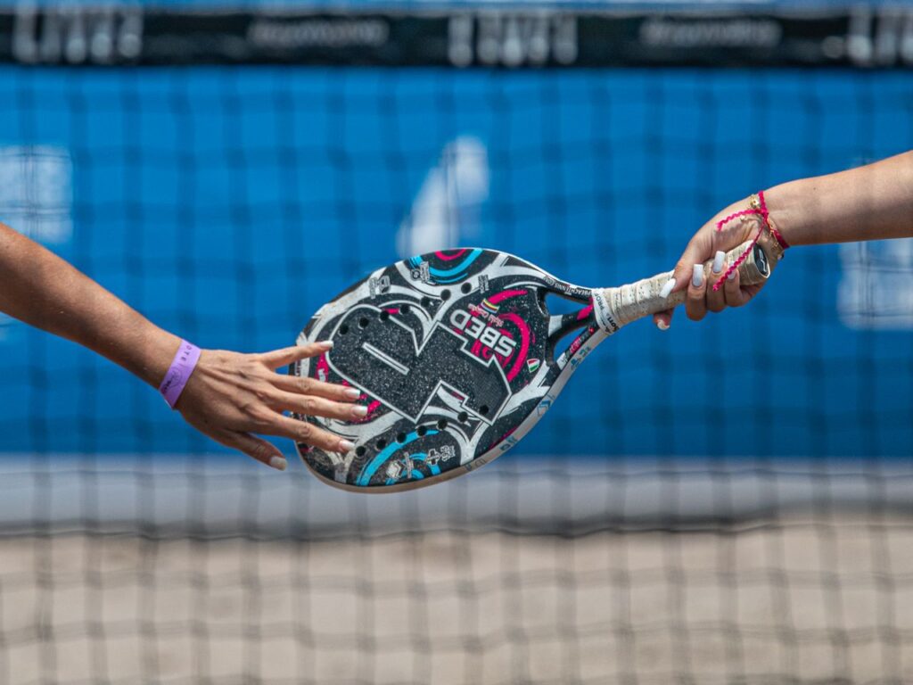 Close-up of two players exchanging a padel racket on an outdoor court.