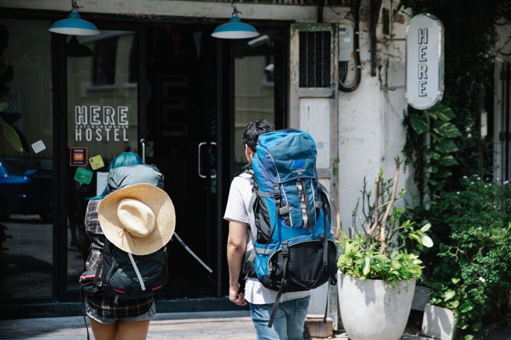 Two backpackers stand at the entrance of a modern hostel, ready for adventure.